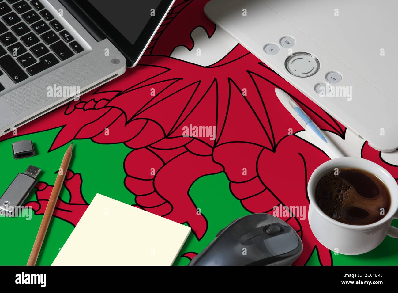 Wales Nationalflagge auf der Draufsicht Arbeitsplatz des kreativen Designers mit Laptop, Computer-Tastatur, usb-Laufwerk, Grafik-Tablet, Kaffeetasse, Maus auf Holz Stockfoto