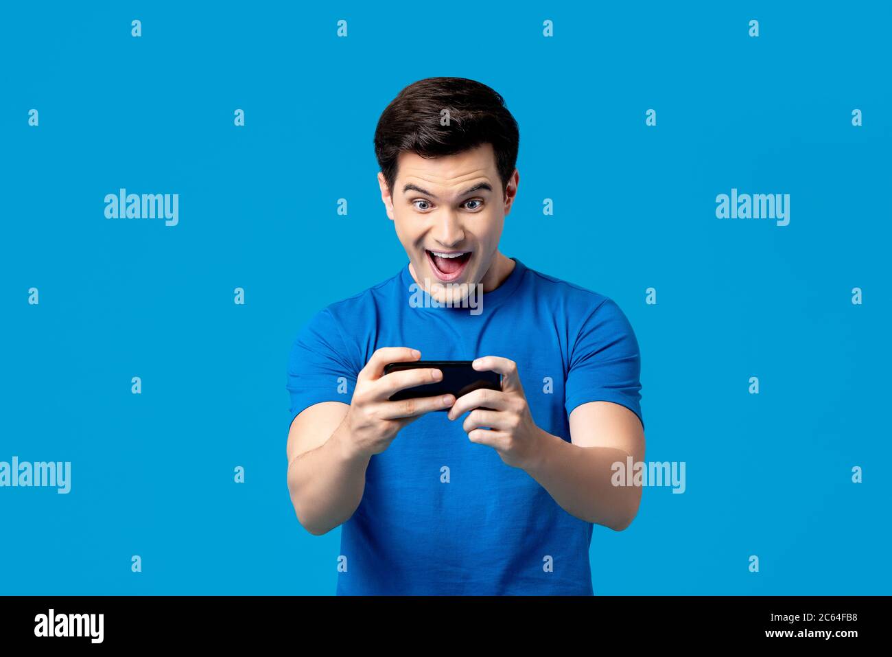 Aufgeregt gut aussehend junge männliche Gamer spielen Online-Spiel auf Smartphone isoliert auf blauem Hintergrund Stockfoto