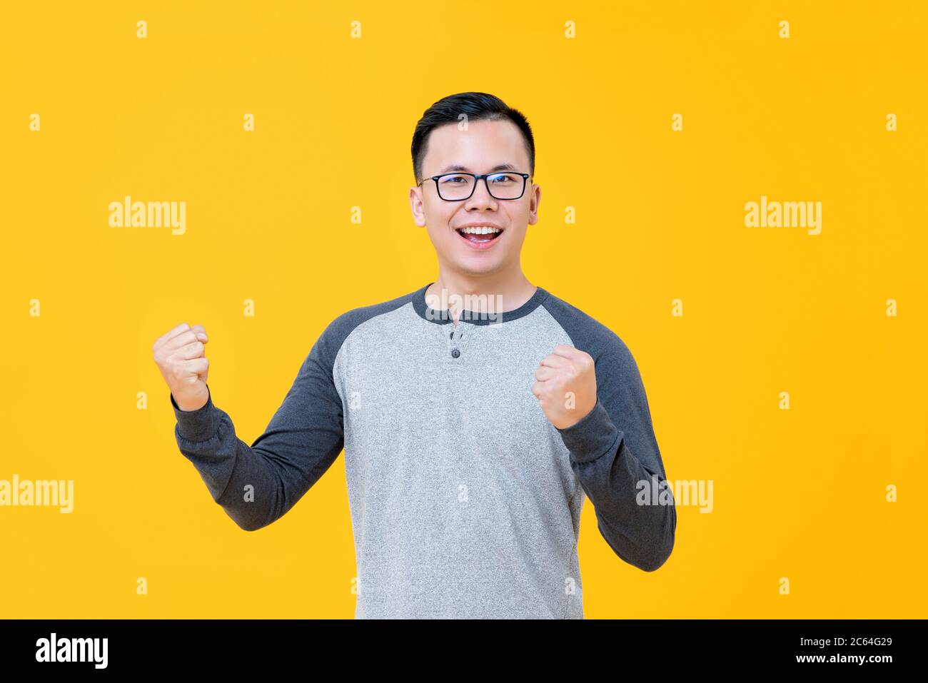 Porträt von glücklich lächelnd asiatischen männlichen Sieger Heben seine Fäuste auf gelbem Hintergrund isloated Stockfoto