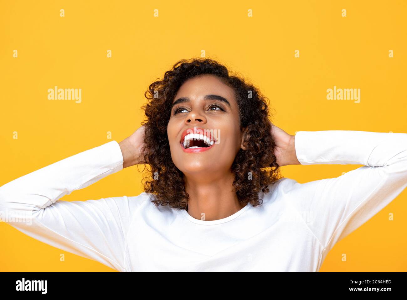 Nahaufnahme Porträt von fröhlichen jungen schönen afroamerikanischen Frau, die mit beiden Armen hinter dem Kopf in isolierten Studio gelben Hintergrund Stockfoto