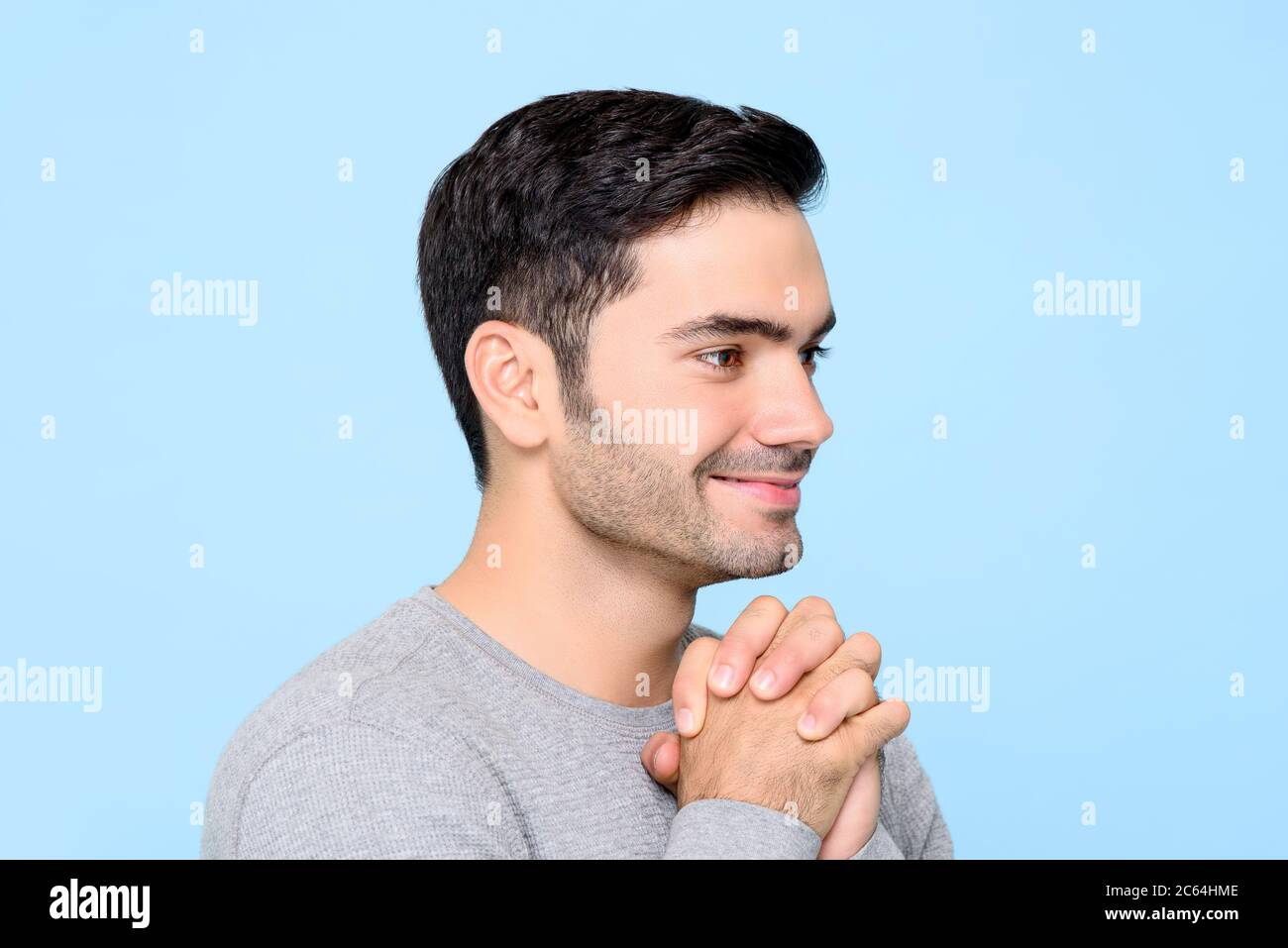 Seitenansicht Porträt eines lächelnden schönen kaukasischen Mann hält seine Hände zusammen mit offenen Augen in isolierten Studio blauen Hintergrund wünschen Stockfoto