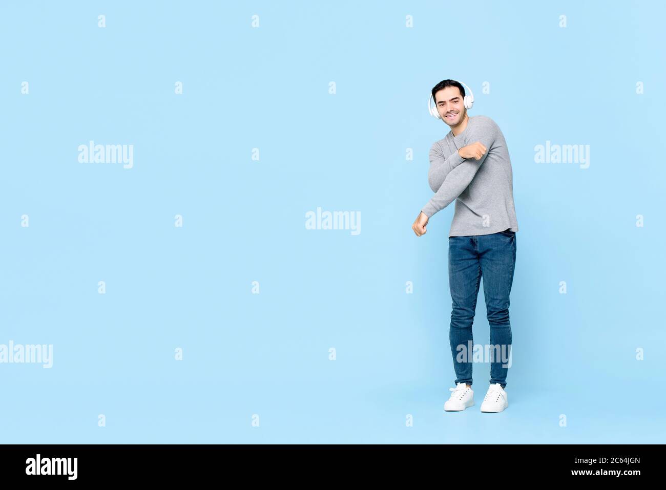 In voller Länge Porträt von lächelnden jungen schönen kaukasischen Mann trägt Kopfhörer Musik hören, während tanzen in isolierten Studio blauen Hintergrund Stockfoto