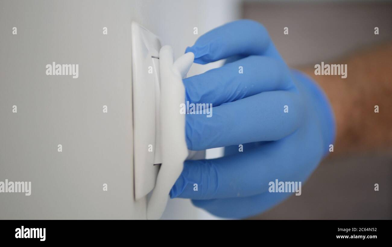 Mann trägt Schutzhandschuhe Reinigung und Desinfektion Licht Schalter aus dem Büroraum mit Desinfektionsmittel gegen Covid-19 Viren Stockfoto