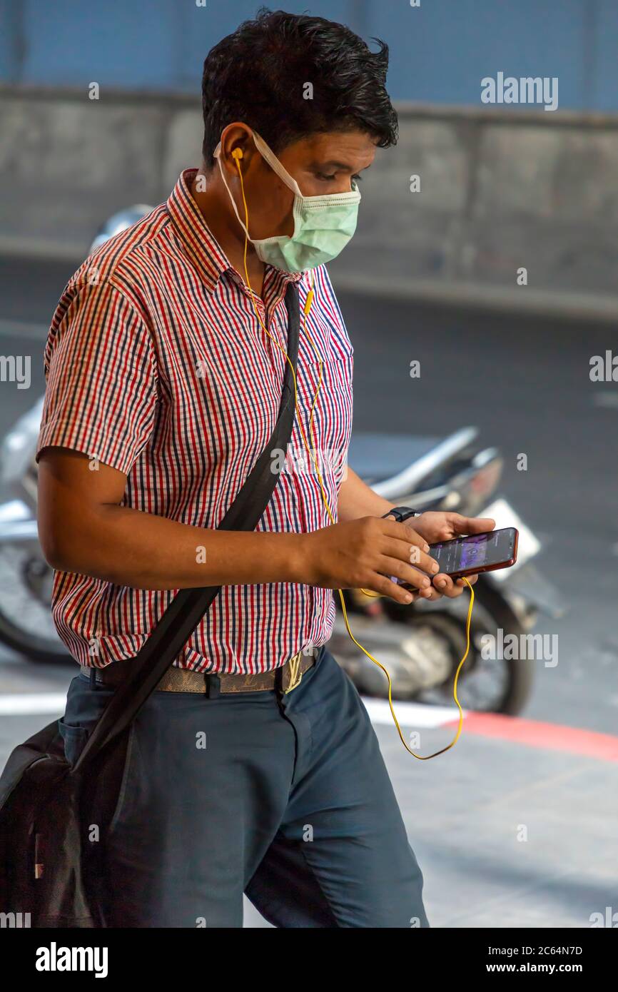 Mann mit Gesichtsmaske und mit Handy während covid 19 Pandemie, Bangkok, Thailand Stockfoto