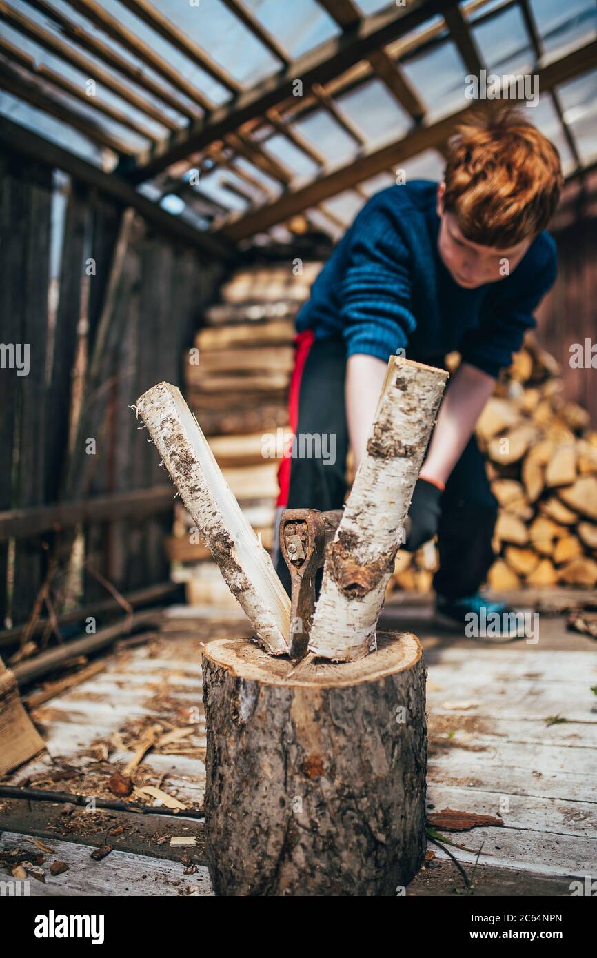 Teen Junge hacken Holz mit einer Axt im Dorf - Ernte Brennholz für den Winter zum Heizen Stockfoto