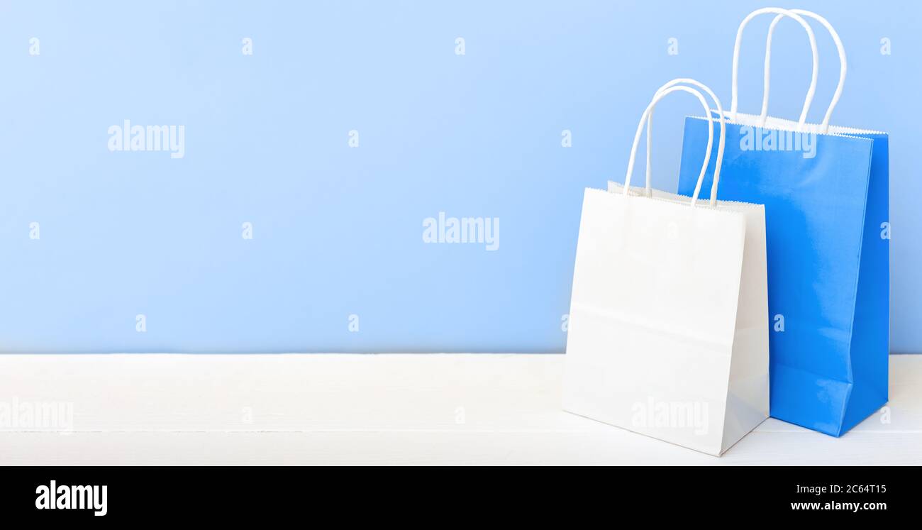 Weiße blaue Handarbeitspapiertaschen. Shopping Mockup Taschen Papier-Pakete auf weißem Tisch blaues Licht Hintergrund mit Kopierraum. Einkaufen, Verkauf, Lieferung von Lebensmitteln Stockfoto