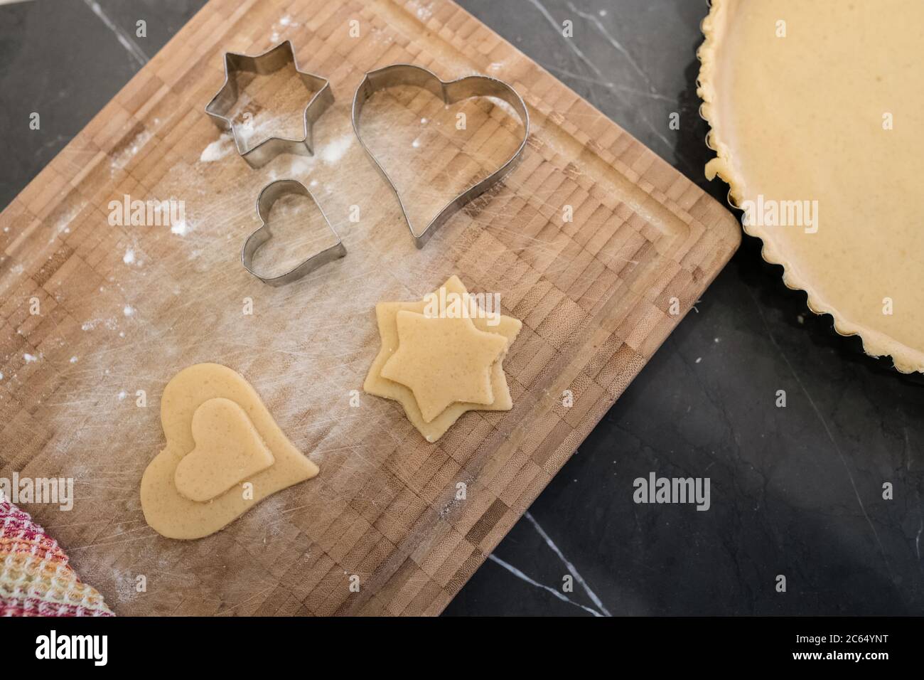 Nahaufnahme von Ausstechformen mit hohem Winkel und Ausschneiden von Teig in Stern- und Herzform auf Holzschneidebrett. Stockfoto