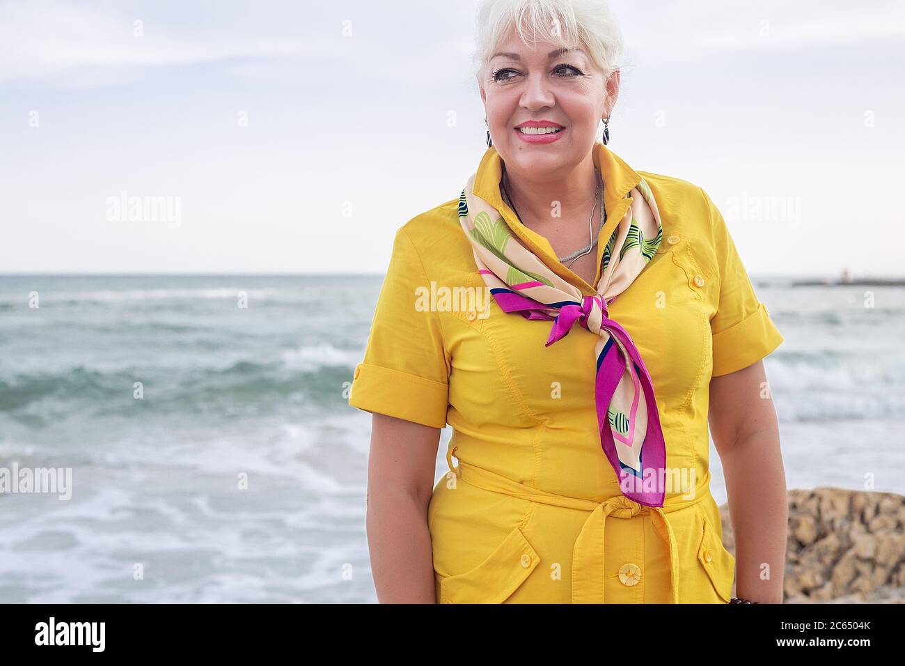 Porträt einer lächelnden Frau, die am Meer steht und ein gelbes Kleid trägt. Stockfoto