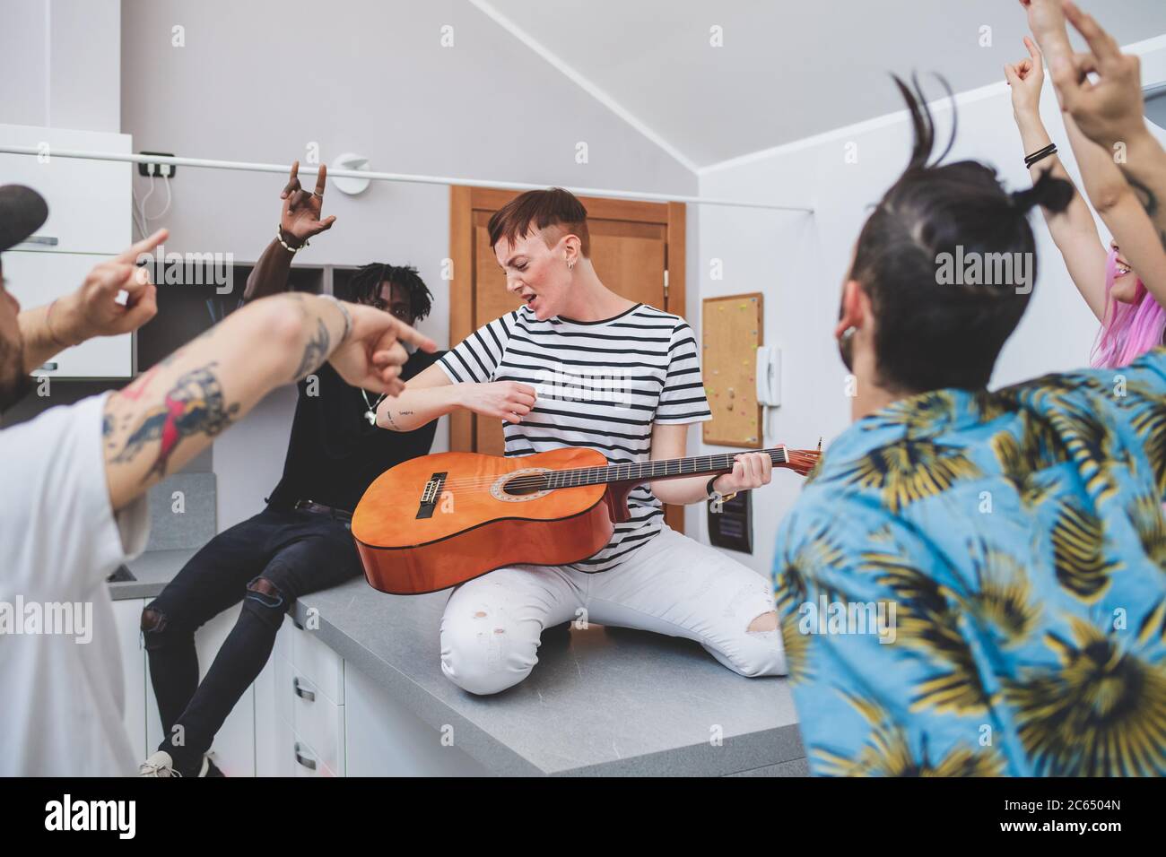 Eine Gruppe junger Männer und Frauen, die eine Hausparty machen, Gitarren und Arme in der Luft spielen Stockfoto