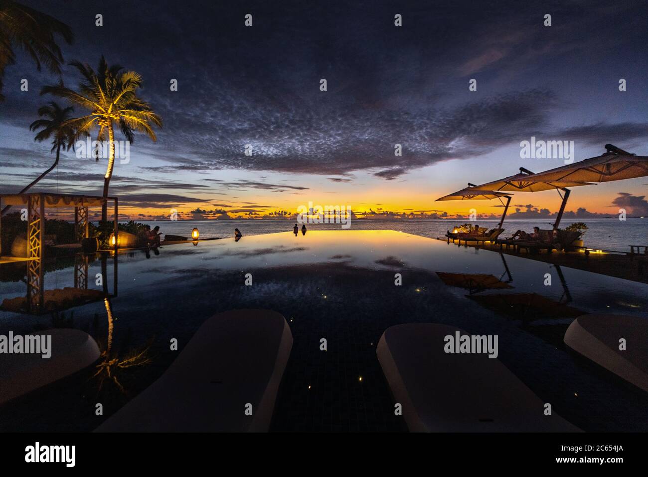 Genießen Sie einen Sonnenuntergang neben einem Infinity-Pool von Inselresorts auf den Malediven, während Sie über die Palmen in den Ozeanhorizont blicken Stockfoto