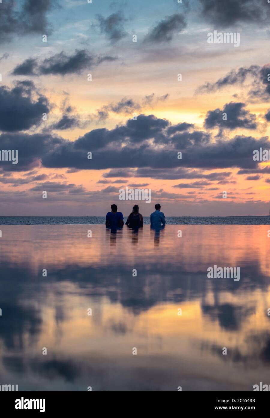 Genießen Sie einen Sonnenuntergang neben einem Infinity-Pool von Inselresorts auf den Malediven, während Sie über die Palmen in den Ozeanhorizont blicken Stockfoto