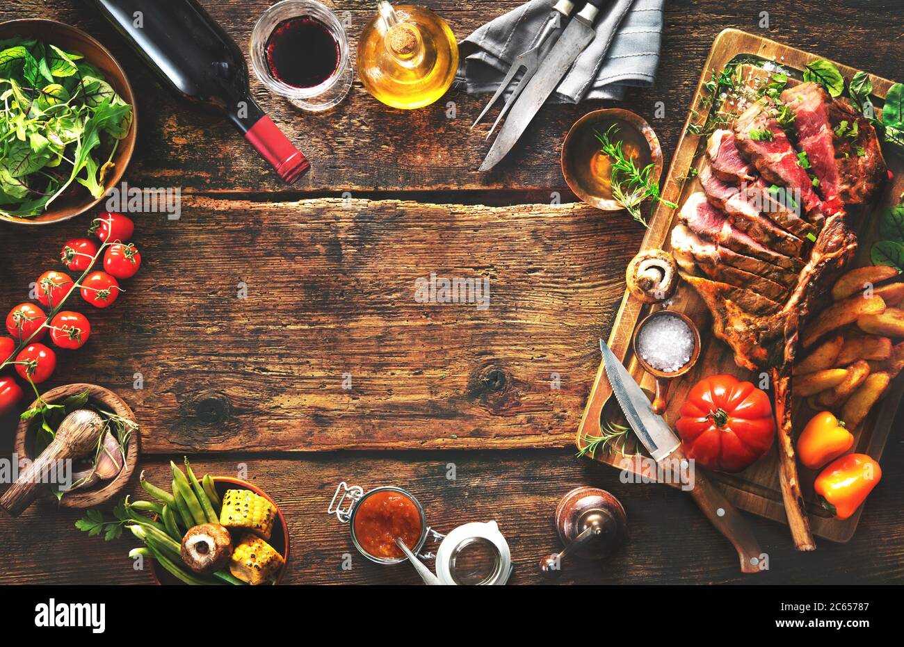 Gegrilltes Fleisch, ​​tomahawk Rindersteak mit Gewürzen, pommes frites und Gemüse auf rustikalem Hintergrund Stockfoto