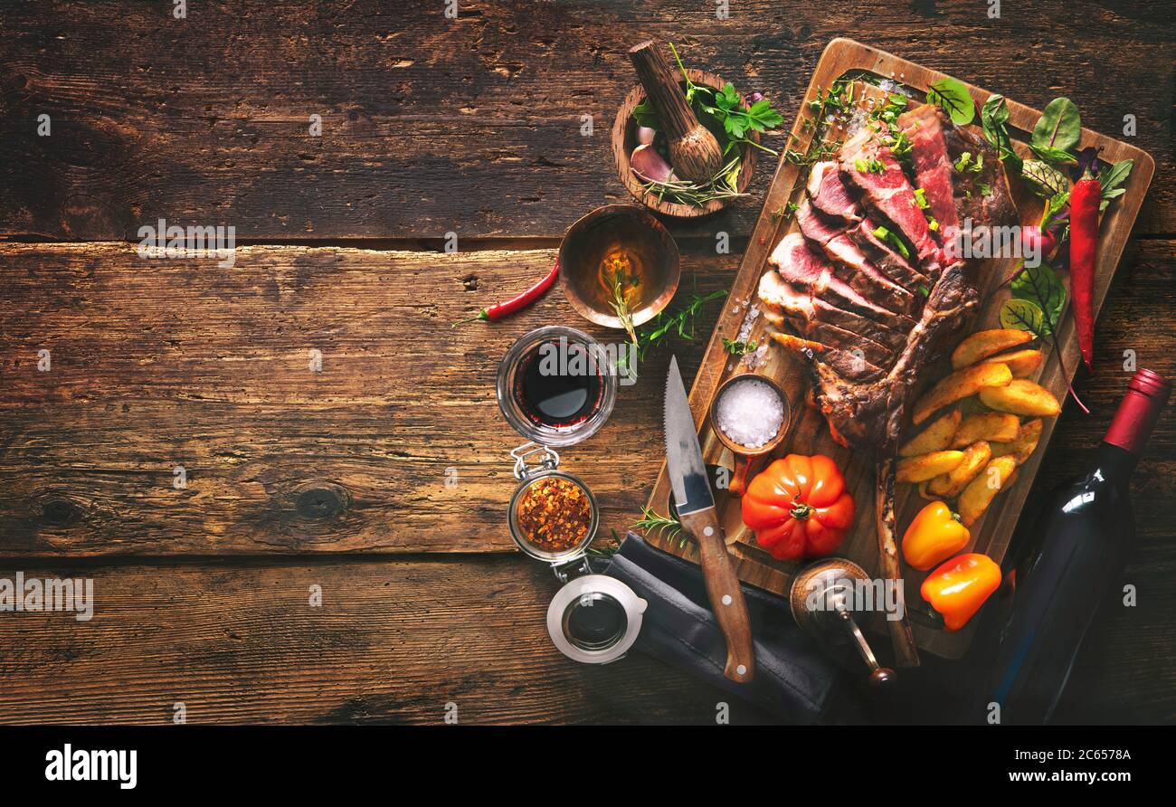 Gegrilltes Fleisch, ​​tomahawk Rindersteak mit Gewürzen, pommes frites und Gemüse auf rustikalem Hintergrund Stockfoto