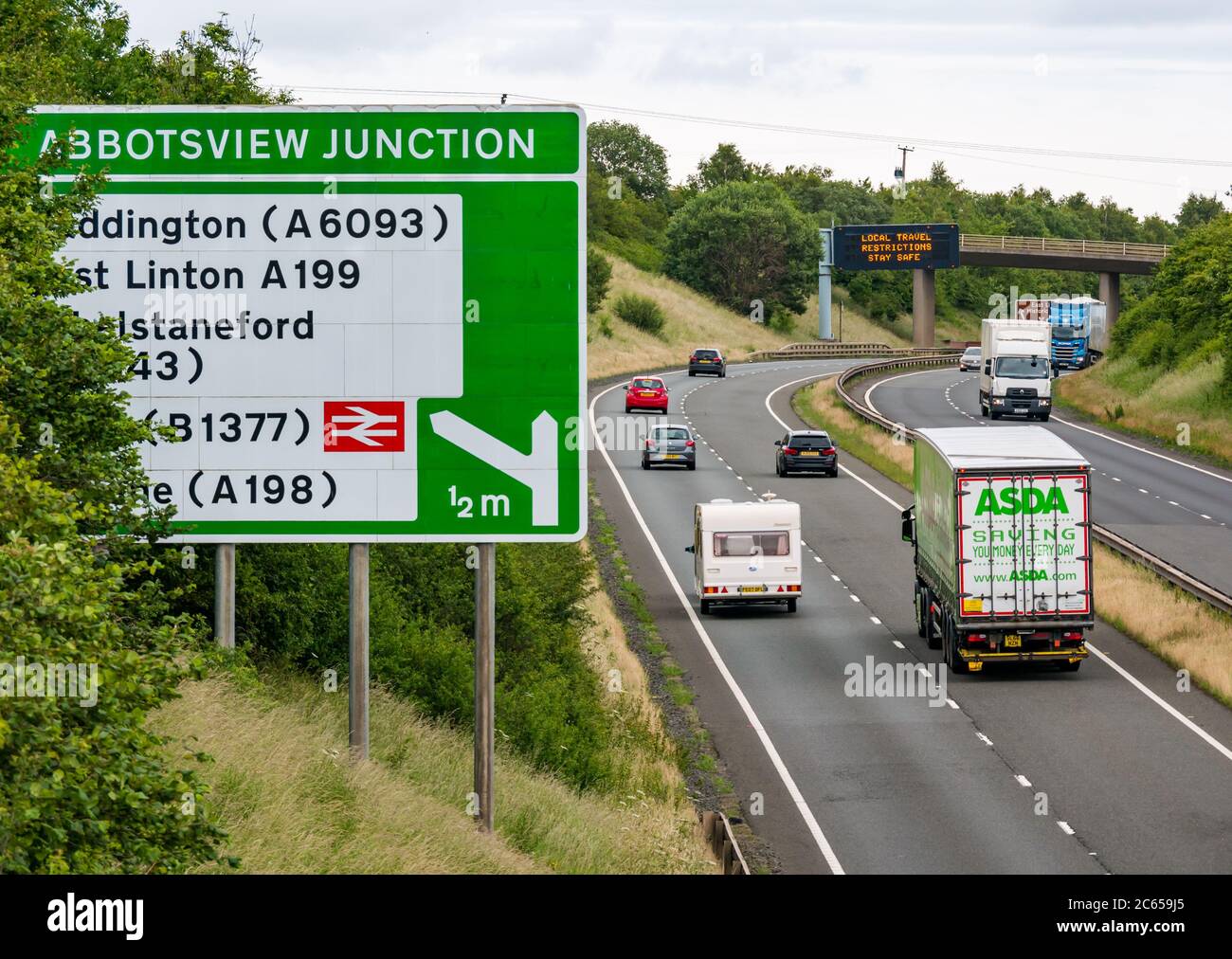 East Lothian, Schottland, Großbritannien, 7. Juli 2020. Covid-19 neue Meldung auf A1-Gantry: Die dritte Version der Pandemie-Meldung erscheint auf der über-Gantry in der Nähe von Haddington, die lautet "Lokale Reisebeschränkungen sicher bleiben", da Schottland in Phase 3, die nächste Woche erwartet wird, eingeht. Der Verkehr auf der zweispurigen Fahrbahn ist viel schwerer als in den letzten Monaten zu sehen war Stockfoto