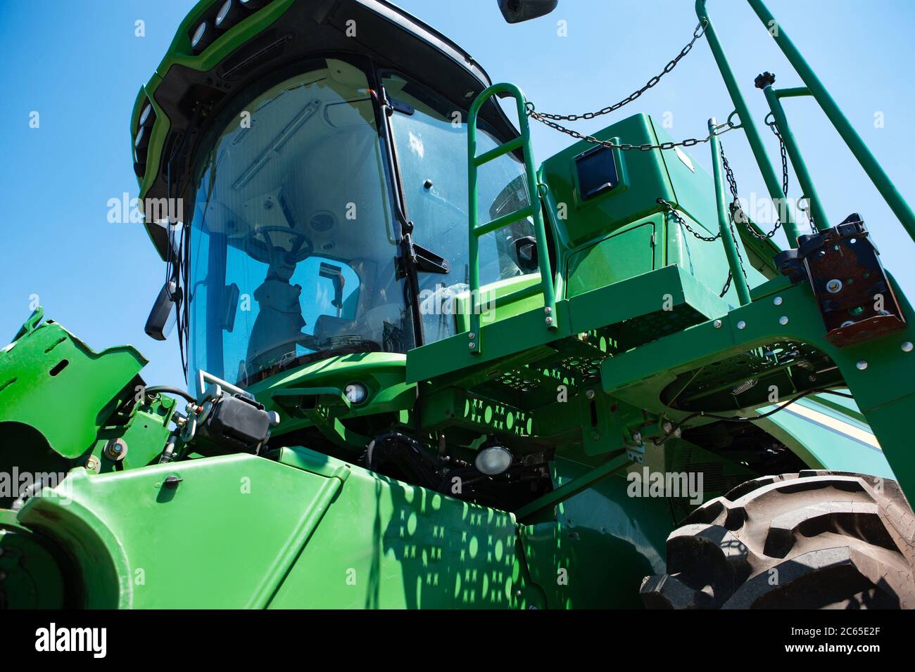 Professionelle moderne Traktor, kombinieren auf einem Feld in Sonnenlicht bei der Arbeit. Lebendige, helle Sommerfarben. Landwirtschaft, Ausstellung, Maschinen, Pflanzenproduktion. Moderne Maschinen am Arbeitsprozess. Stockfoto