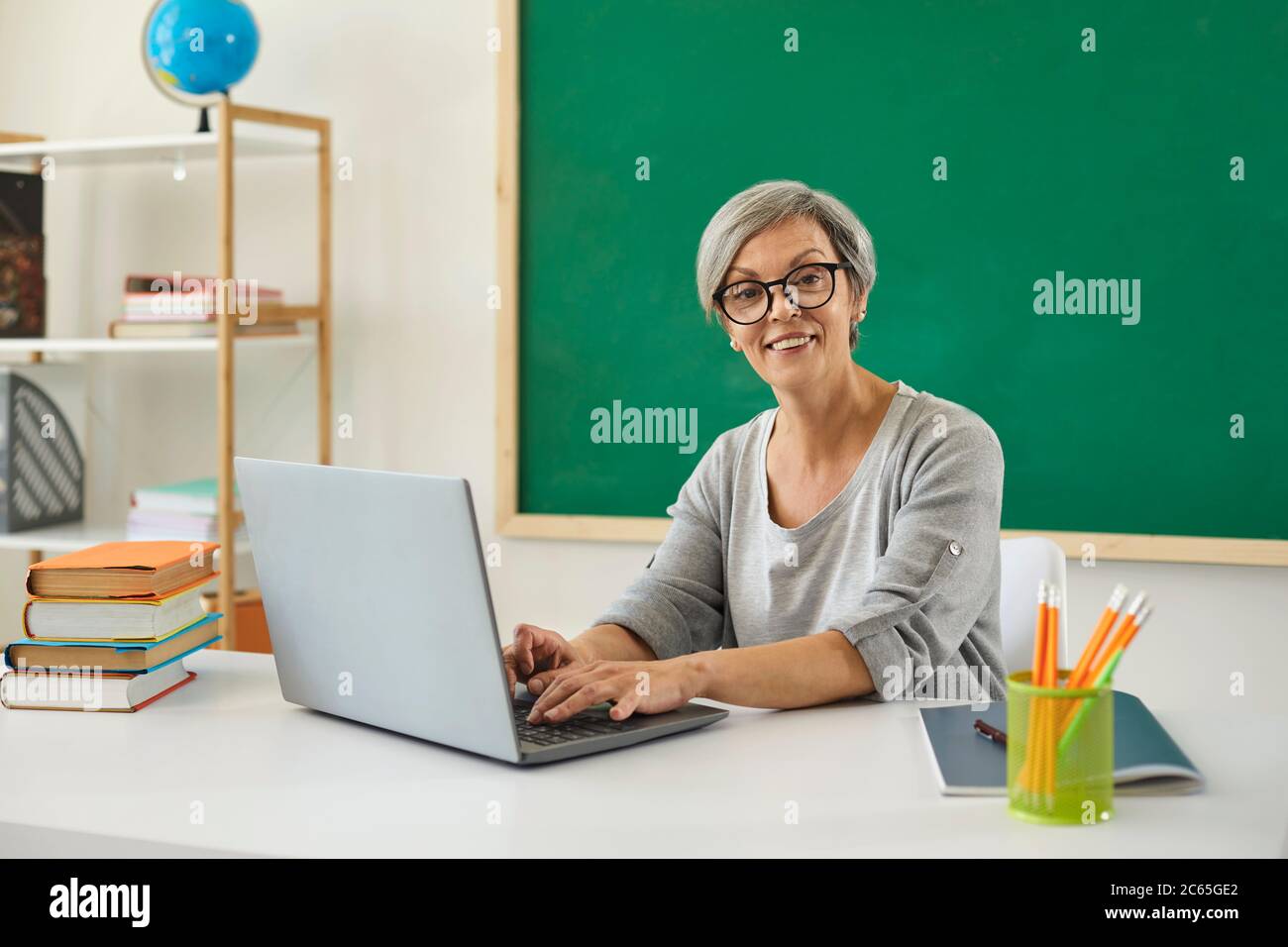 Lehrer Schule Universität online. Frau Oberlehrerin spricht mit Schülern hat Web-Chat mit Laptop-Computer sitzen am Schreibtisch im Klassenzimmer. Stockfoto