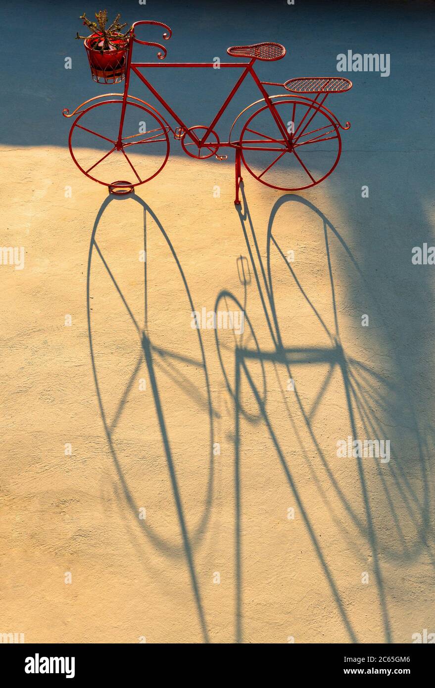 Ein dekoratives rotes Fahrrad mit einem langen Schatten bei Sonnenuntergang in Santorini, Griechenland Stockfoto