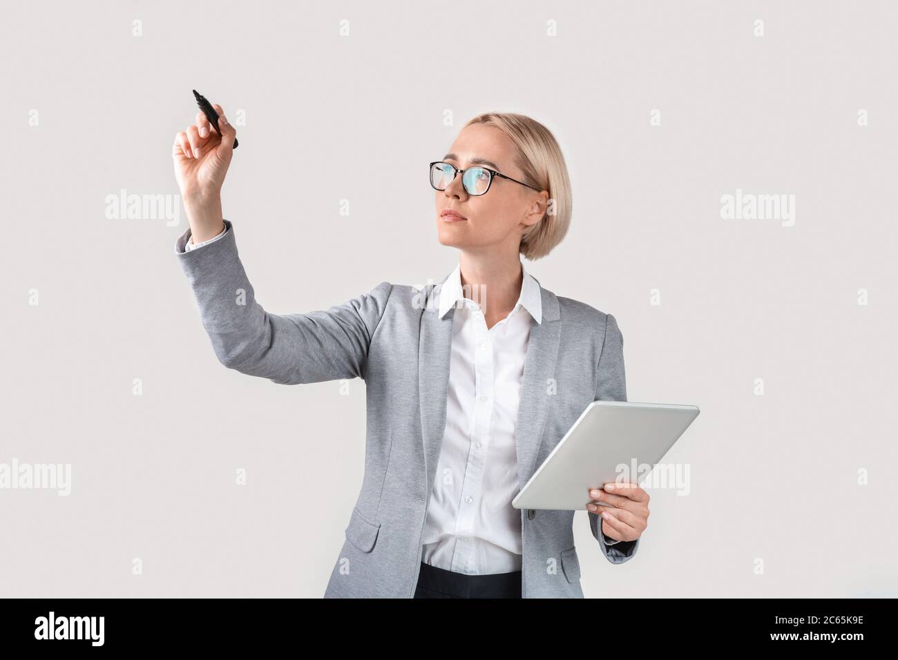 Smart Geschäftsfrau mit Tablet schreiben etwas auf imaginären Bildschirm vor hellem Hintergrund, mockup für Design Stockfoto