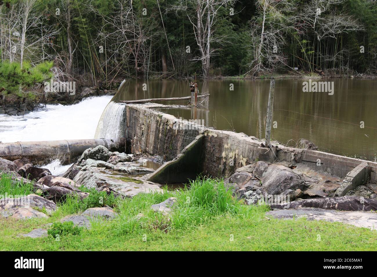 Ein sehr alter Damm Wehr in der Nähe eines Grasfeldes mit Wald dahinter Stockfoto