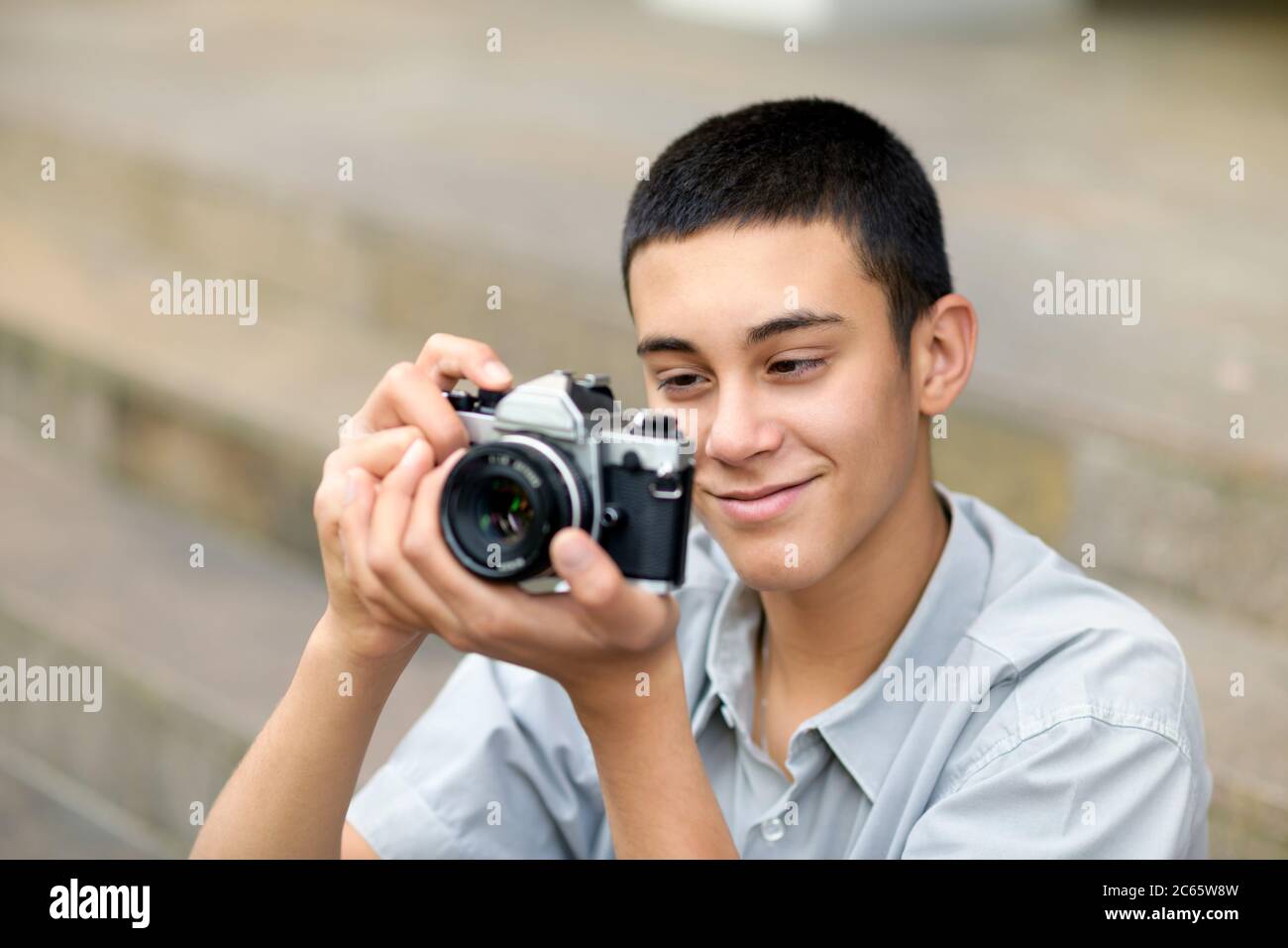 Junger Teenager mit einer alten Kamera, während er seine Aufnahme auf dem Rückschirm mit einem erfreuliches Lächeln in der Nähe prüft Stockfoto