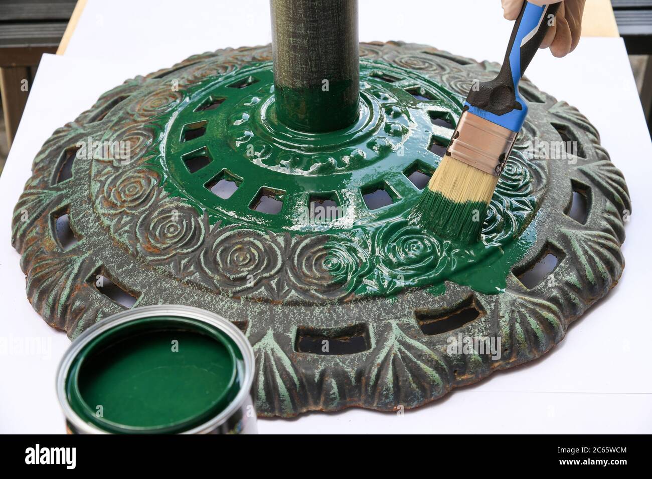 Person Malerei eine verzierte kreisförmige Gusseisen Basis mit grüner Farbe in einer Nahaufnahme auf den geöffneten Topf von Pigment und Pinsel in einem DIY-Konzept Stockfoto