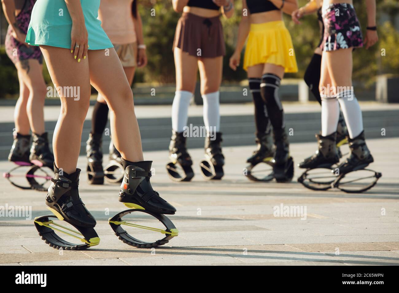 Nahaufnahme Frauen in Sportbekleidung Springen in einem kangoo Jumps Schuhe  auf der Straße am sonnigen Sommertag. Springen hoch, aktive Bewegung,  Action, Fitness und Wellness. Passen Sie weibliche Modelle während des  Trainings an
