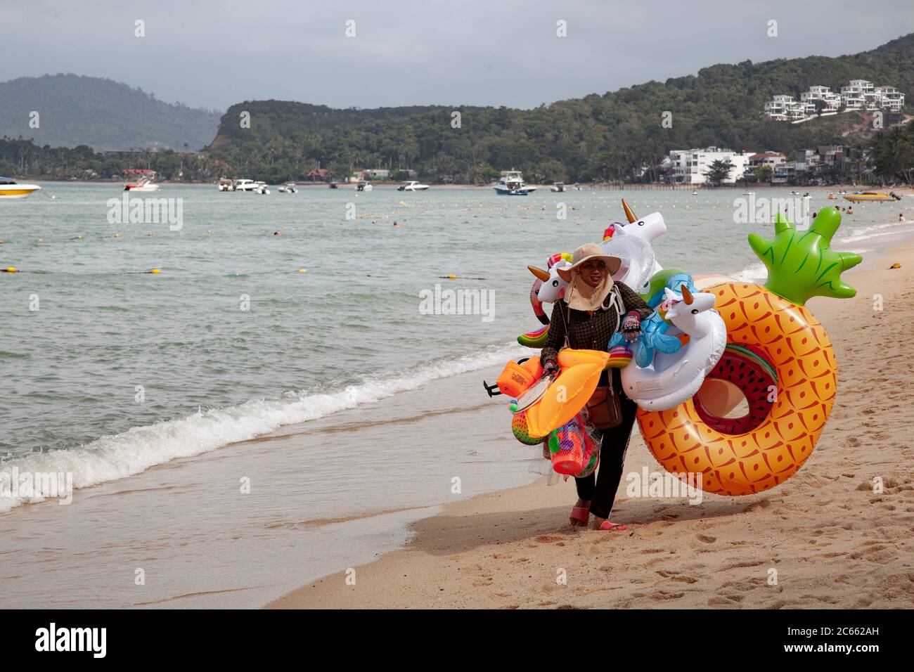 Weibliche Strandverkäufer, die auf dem Sand mit einer Reihe von bunten Schlauchboote, einschließlich Gummiringe, zum Verkauf in Koh Samui, Thailand, spazieren Stockfoto