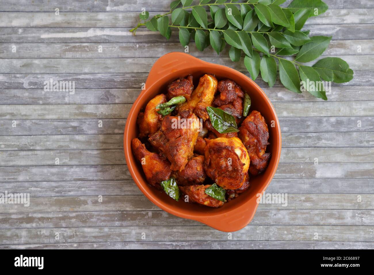 Hähnchenbraten oder gebratenes Hähnchenkabab, das gut mit Curryblättern in einer schwarzen Bratpfanne mit grauem Hintergrund oder erdernem Waren garniert wird Stockfoto