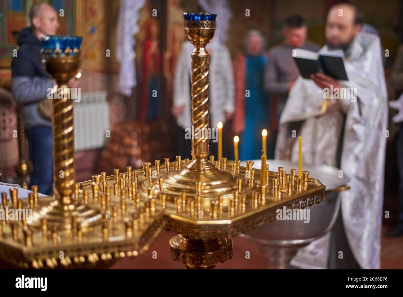 Kerzen in einem großen goldenen Kronleuchter in der orthodoxen Kirche, Nahaufnahme, Priester mit Gemeindemitgliedern im Hintergrund aus der Blickweite Stockfoto