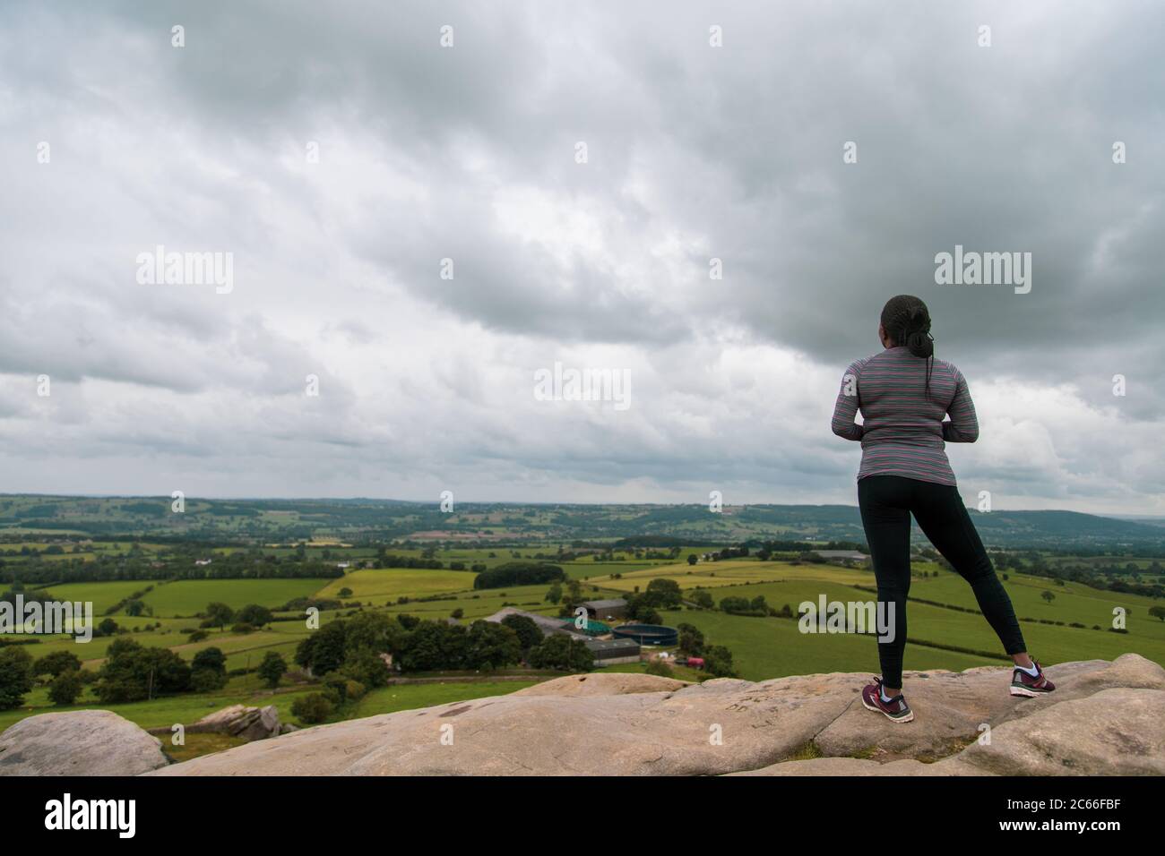 Eine schwarze Frau, die auf einem Felsen steht und den wolkigen Horizont in sportlicher Kleidung betrachtet Stockfoto