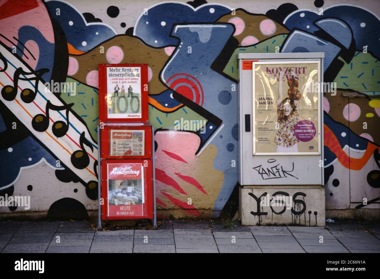 Ein Zeitungsstand der Abendzeitung und eine elektrische Verteilbox mit Veranstaltungsplakat vor einer bunten Graffiti-Wand in München, Stockfoto
