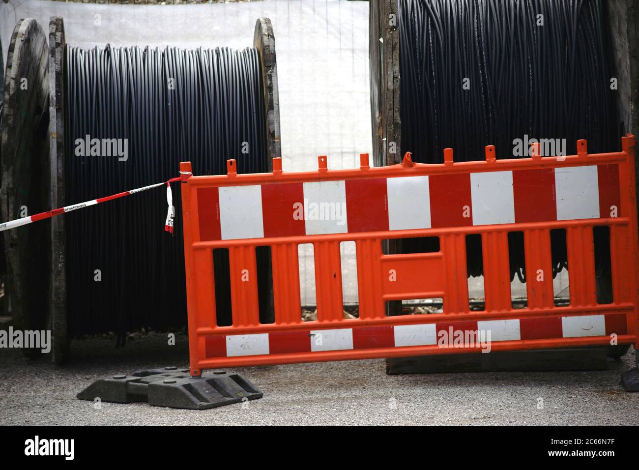 Große Holzkabelspulen mit elektrischen Kabeln hinter einer Straßenbarriere, Stockfoto