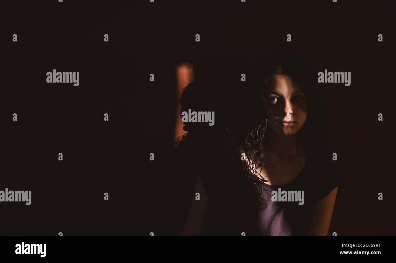 Junge Frau auf schwarzem Hintergrund mit Licht und Schatten an Gesicht Stockfoto