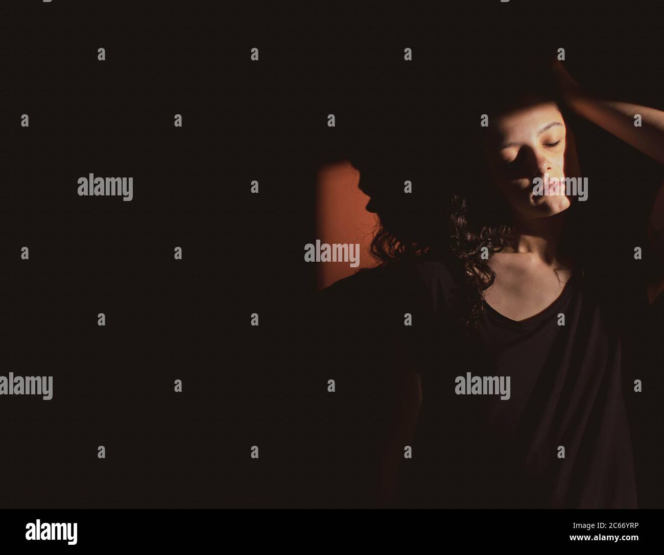 Junge Frau auf schwarzem Hintergrund mit Licht und Schatten an Gesicht Stockfoto