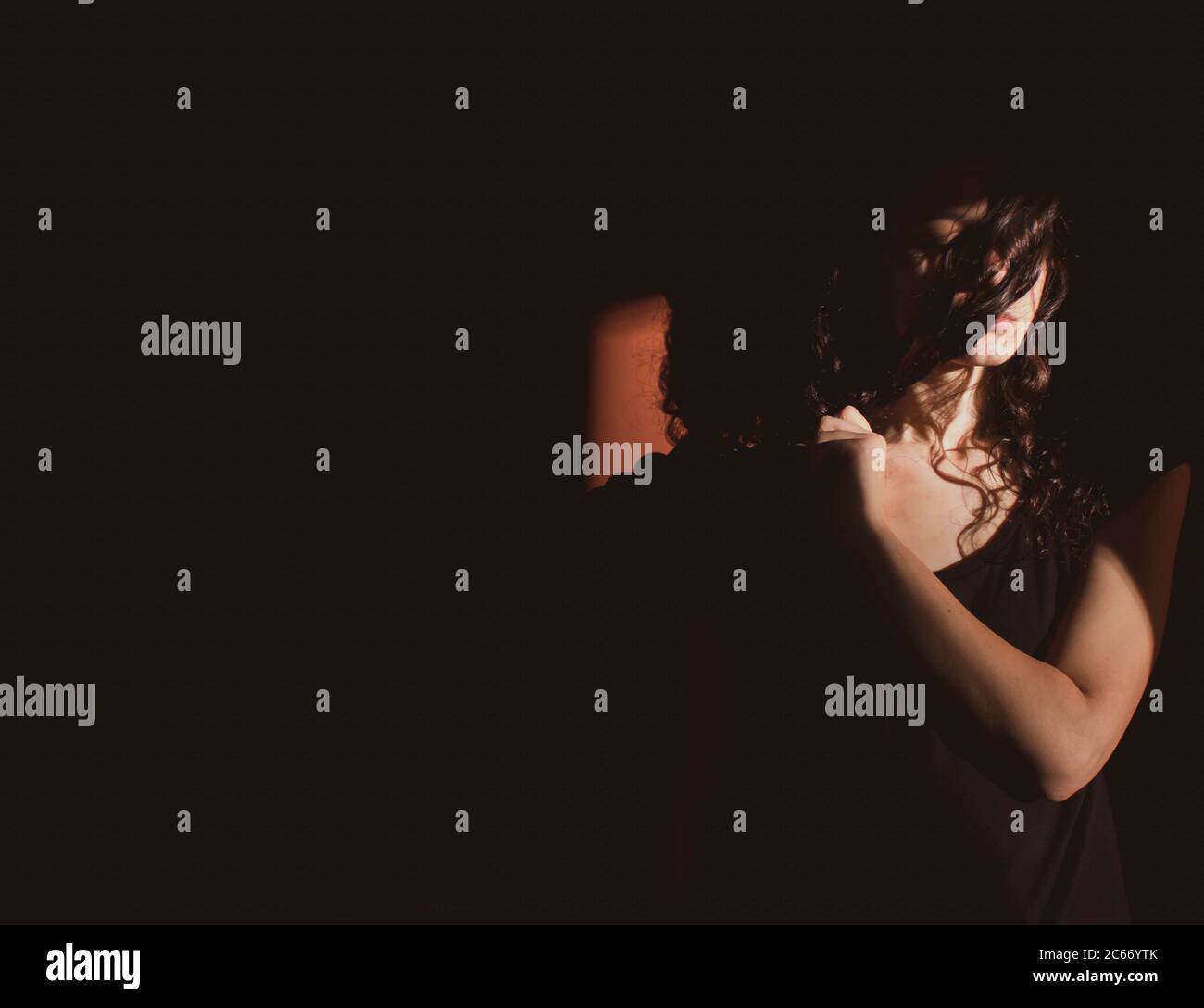 Junge Frau auf schwarzem Hintergrund mit Licht und Schatten an Gesicht Stockfoto