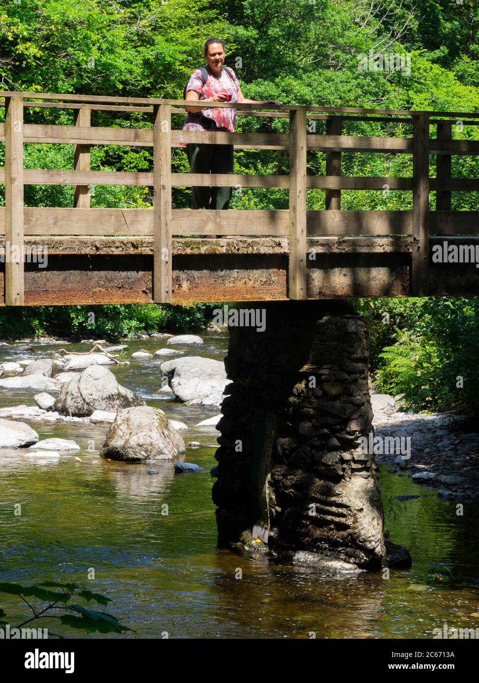 Frau, die auf einer Fußgängerbrücke über Hoar Oak Water, Watersmeet, Devon, Großbritannien, steht Stockfoto