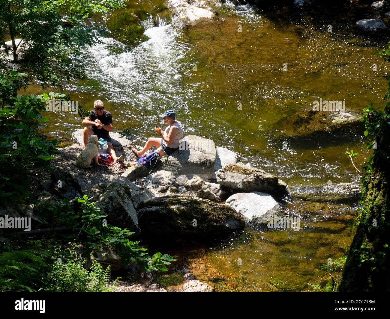 Ein Paar mittleren Alters saß auf Felsen am East Lyn River und hatte ein Picknick, Devon, Großbritannien Stockfoto