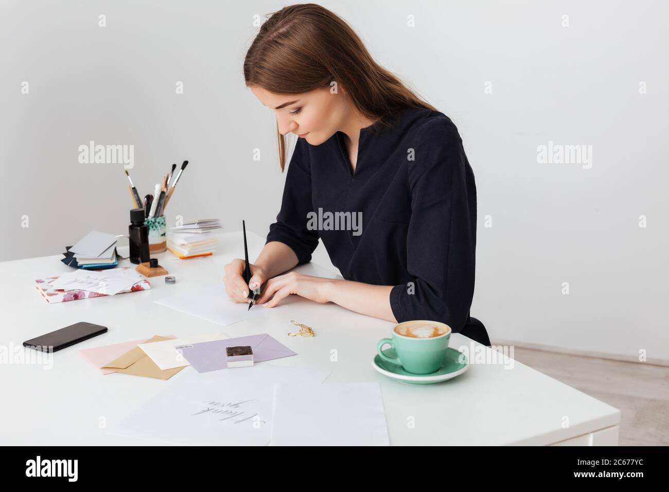 Portrait einer jungen schönen Dame, die mit einer Tasse Kaffee am weißen Schreibtisch sitzt und auf Papier isoliert schreibt Stockfoto