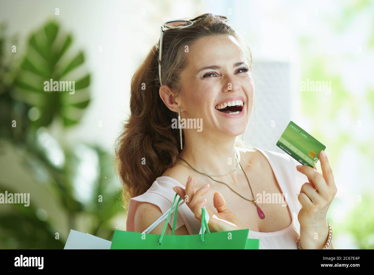 Lächelnd elegante 40 Jahre alte Frau Shopper in rosa Bluse mit Kreditkarte und Papier Einkaufstaschen. Stockfoto