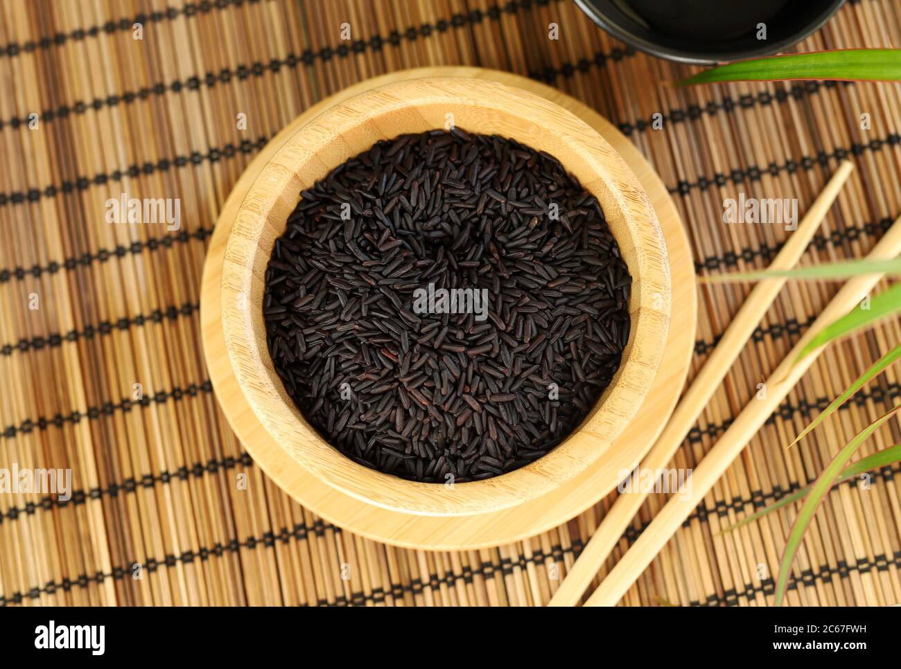 Gesundes Lebensmittelkonzept. Schwarzer Wildreis mit Essstäbchen in einer Holzschüssel auf einer Bambusmatte. Selektiver Fokus. Blick von oben. Stockfoto