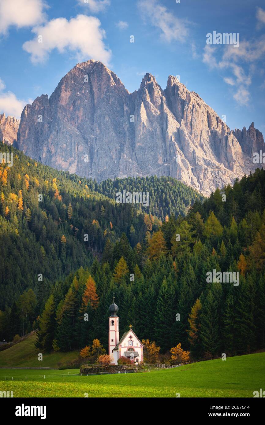 Die Kirche von San Giovanni in Ranui mit dahinter einem Wald mit Lärchen in Herbstfarben und einem Dolomitengipfel in Sankt Magdalena, Italien. Stockfoto