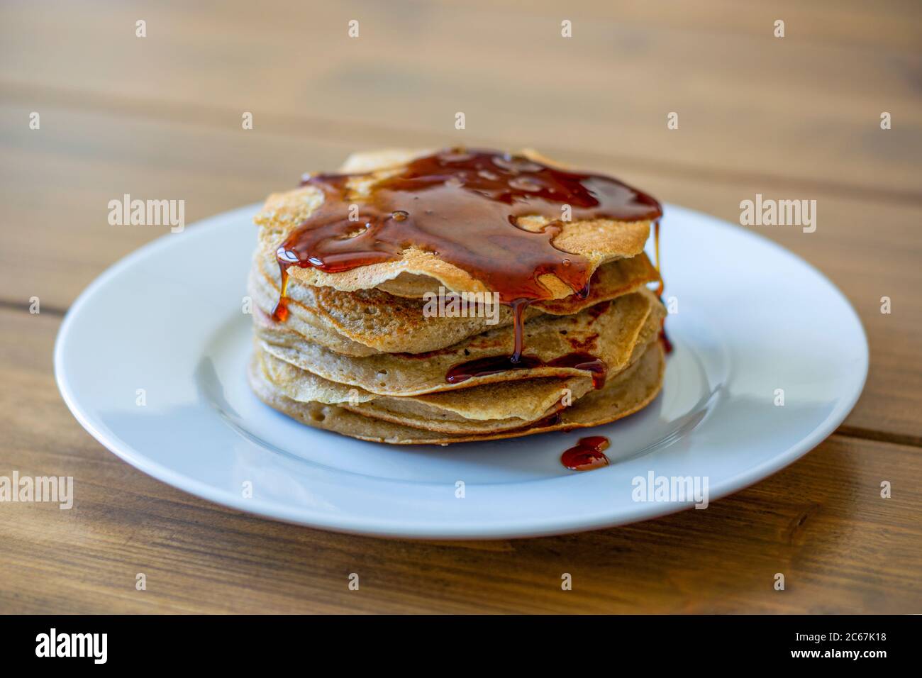 Stapel von hausgemachten einfachen amerikanischen Stil Pfannkuchen mit goldenem Sirup über sie auf Holztisch gegossen Stockfoto