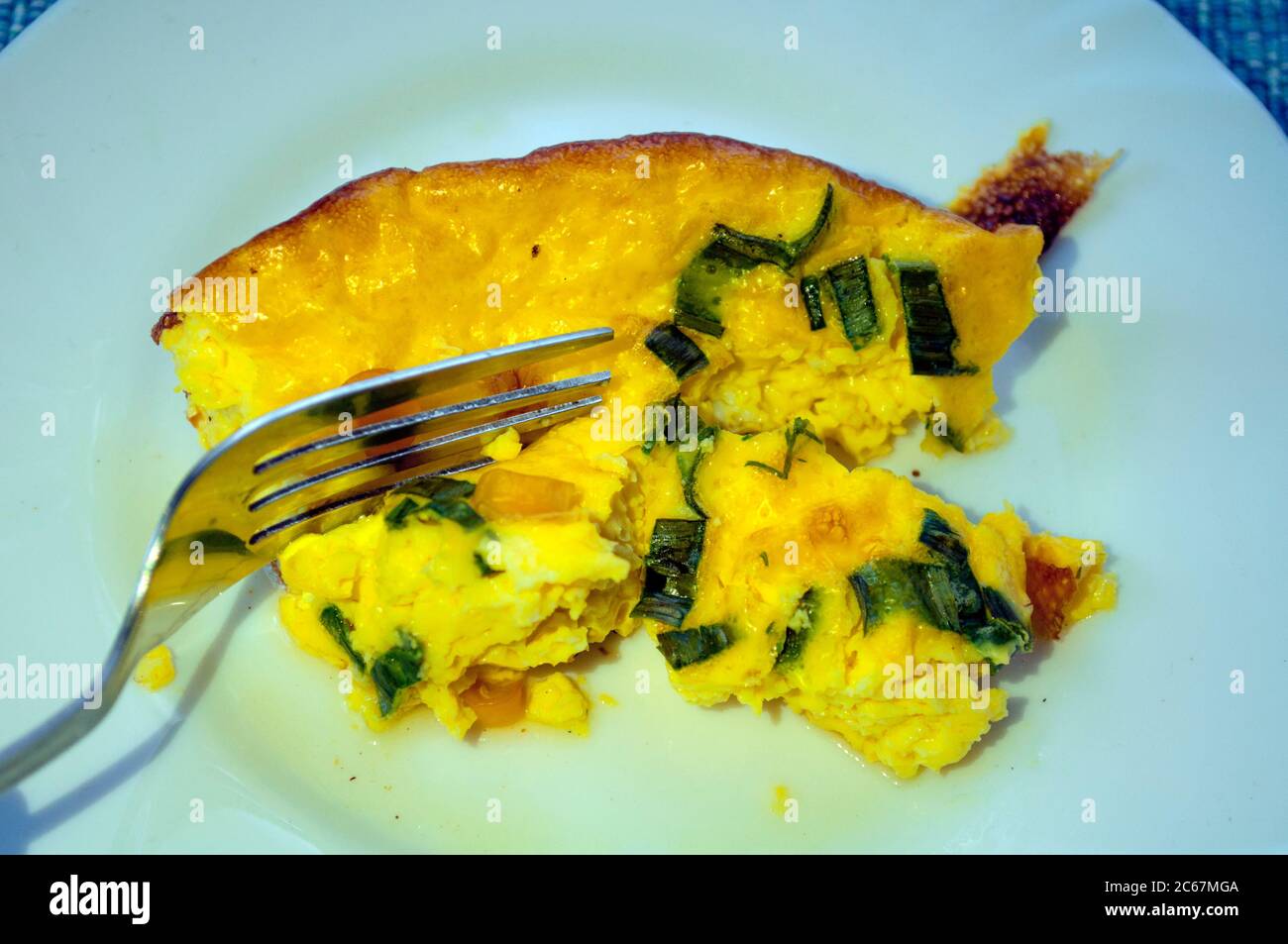 Auf einer weißen Platte Portion gelbes Omelett mit Grüns und Mais. Gabel auf der linken Seite, Linkshänder Stockfoto