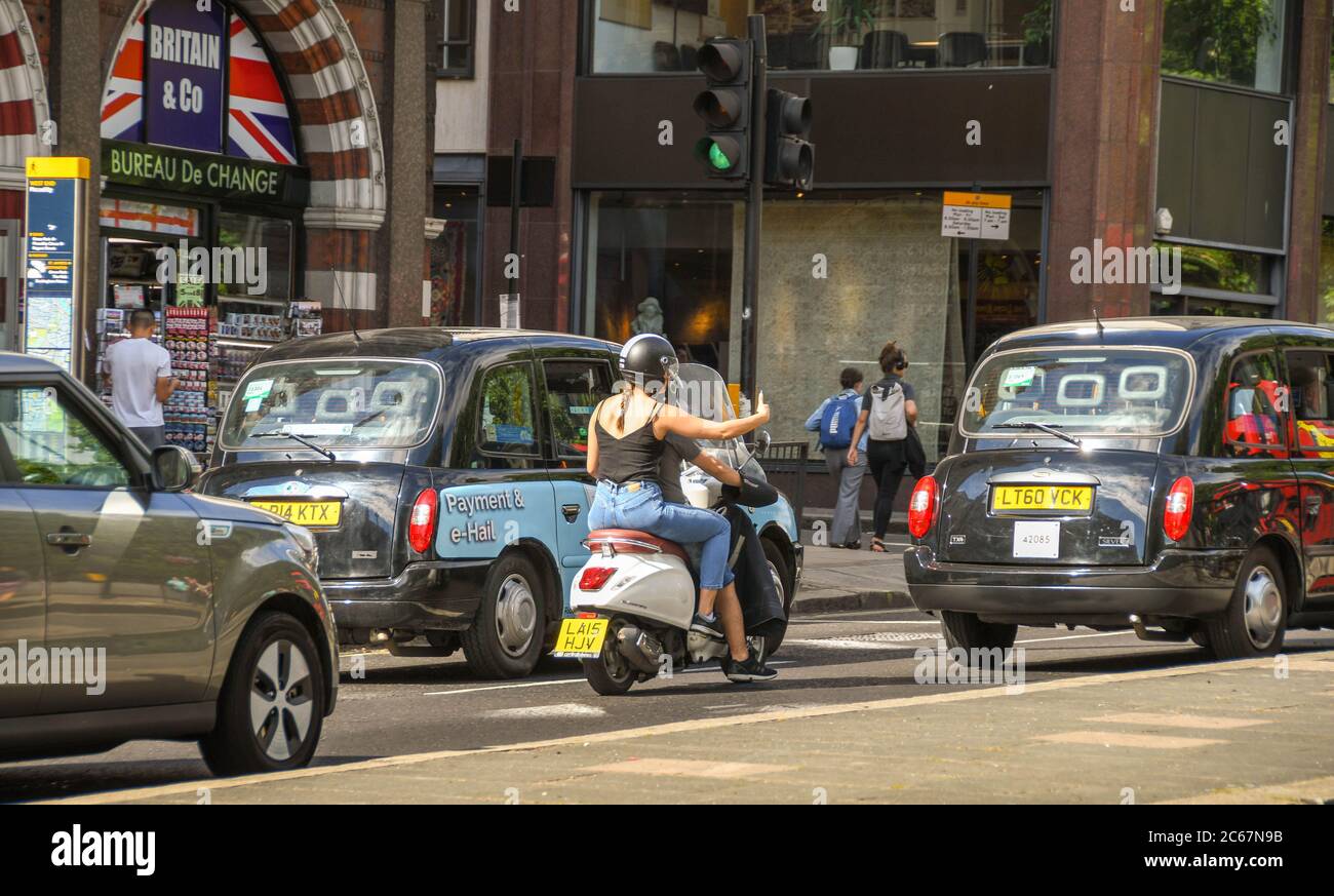 London, England - Juli 2018: Junge Frau auf einem Motorroller auf Pillion, die Selfies macht, während sie eine Straße im Zentrum Londons entlang fährt. Stockfoto