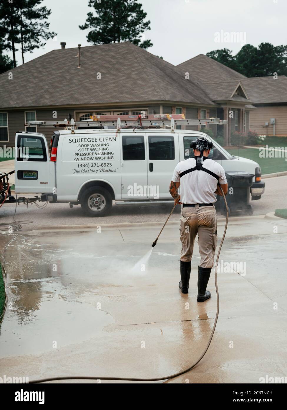 Man Druckwäsche oder Powerwashing oder Reinigung einer Betoneinfahrt und Bürgersteig in Montgomery Alabama, USA. Stockfoto