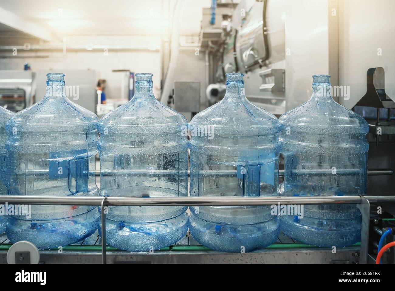 PET-Flaschen oder Gallonen aus Kunststoff auf Produktionslinie oder Förderband in der Wasserfabrik zum Abfüllen von reinem Trinkwasser. Stockfoto