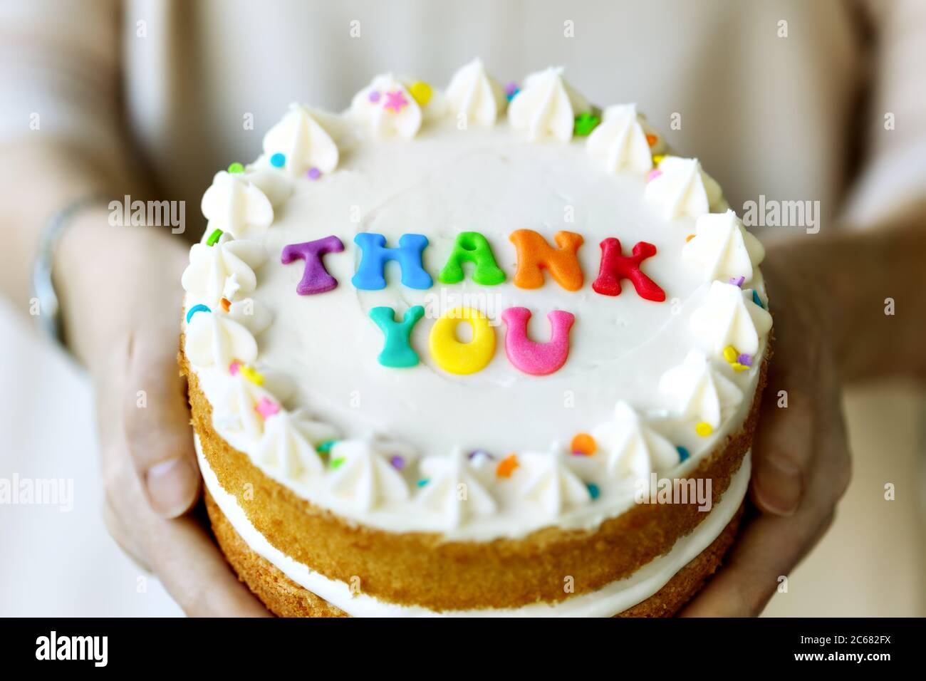 Hände halten Kuchen mit bunten Regenbogen Buchstaben Rechtschreibung danke Stockfoto