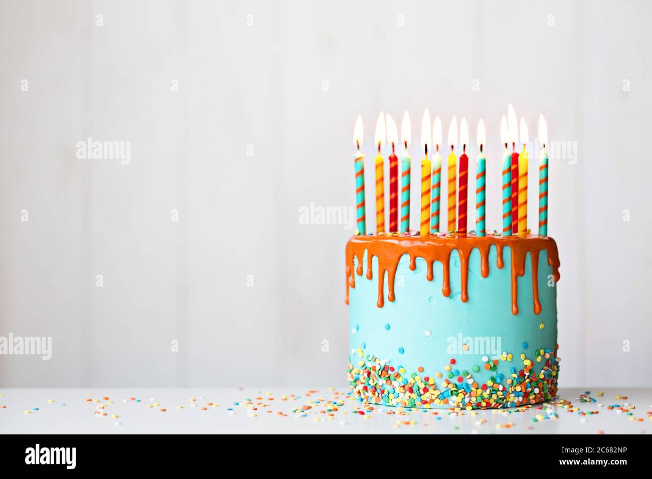 Bunte Geburtstagstorte mit vielen Kerzen und Orangentropfvereisung Stockfoto