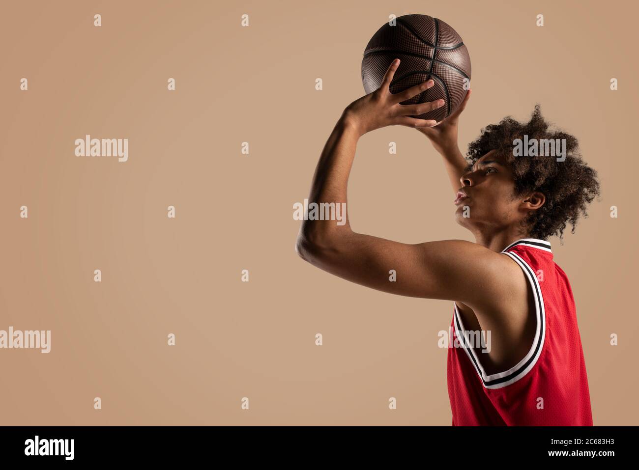 Basketballspieler wirft den Ball auf braunen Hintergrund. Stockfoto