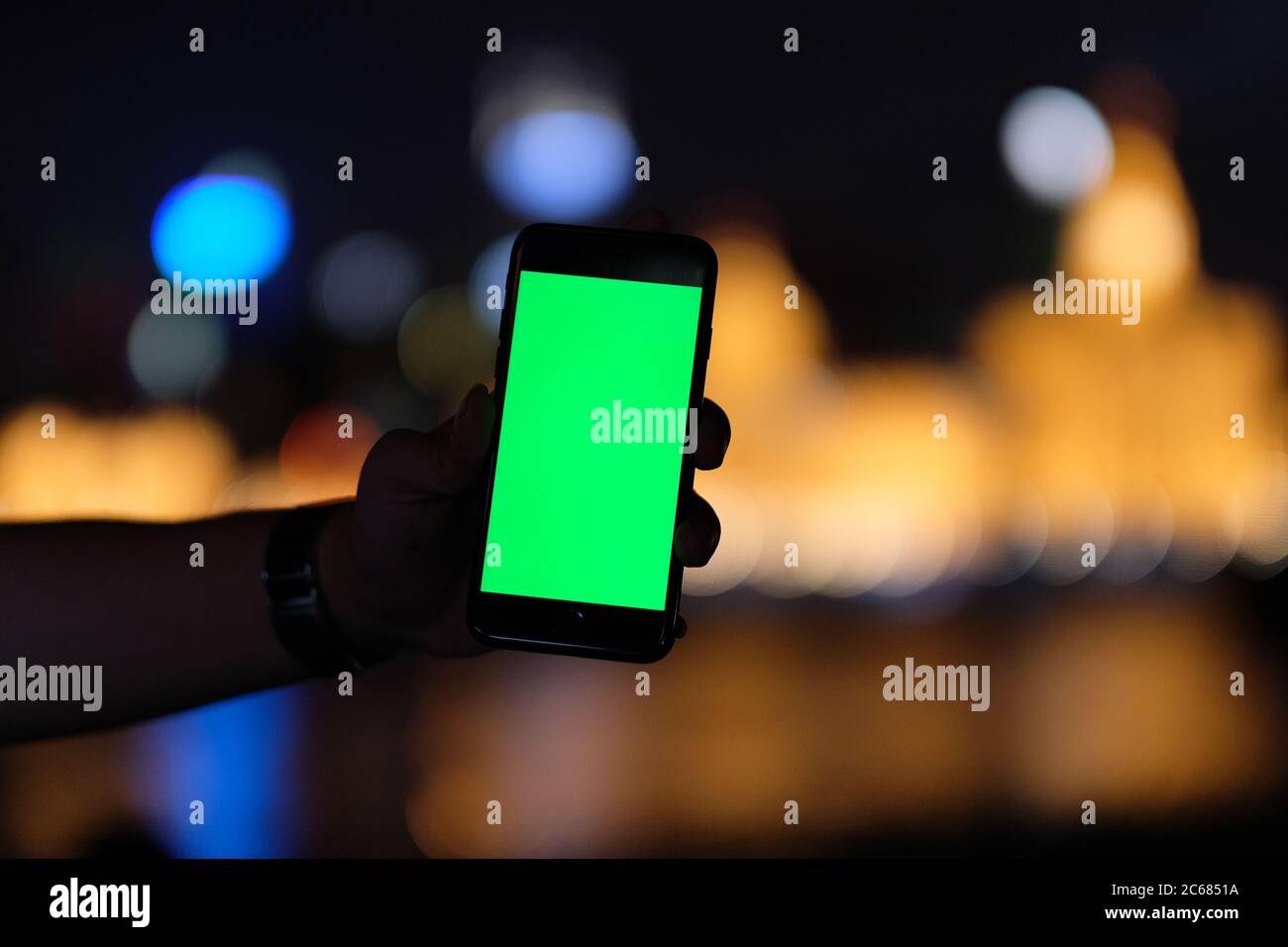 Eine Hand Silhouette zeigt grünen Bildschirm Smartphone in der dunklen Nacht. Schöne verwischen goldenen Stadtlichter Hintergrund Stockfoto